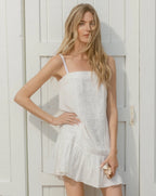 A blonde woman in a white dress stands in front of a white wooden door.