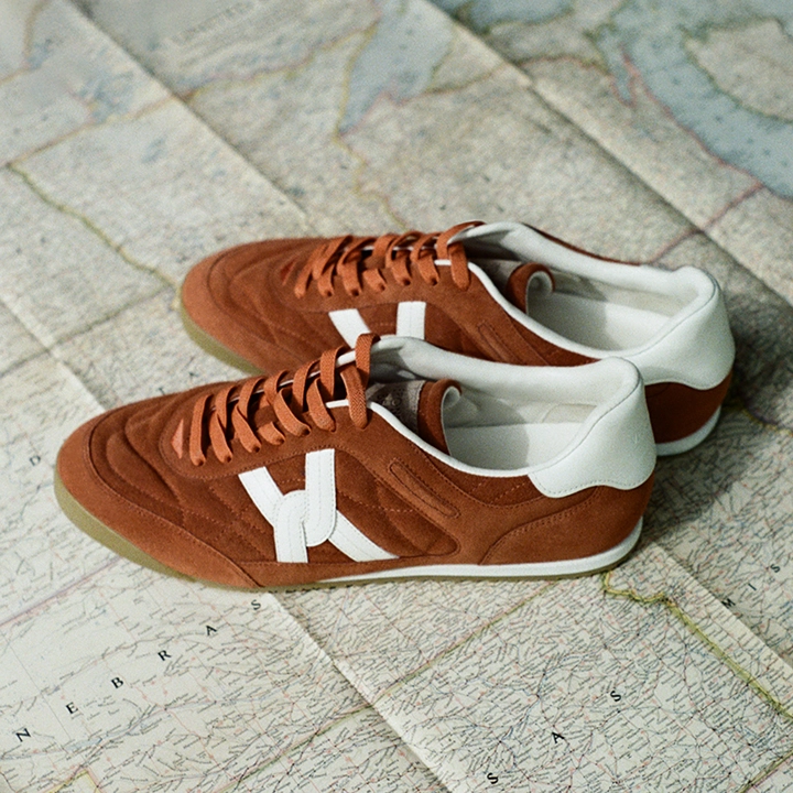 A pair of brown suede sneakers with white accents rests on a vintage map.
