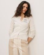 Veronica Beard Off-white button-front cardigan with "STRESS DOESN'T GO WITH MY OUTFIT" embroidered on the chest.