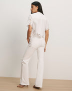Veronica Beard White eyelet lace short-sleeve button-up shirt with scalloped hem and white flare jeans.
