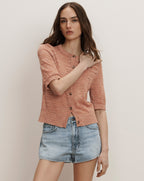 Veronica Beard A peach-colored knit cardigan with short sleeves and brown buttons, paired with light wash denim shorts.