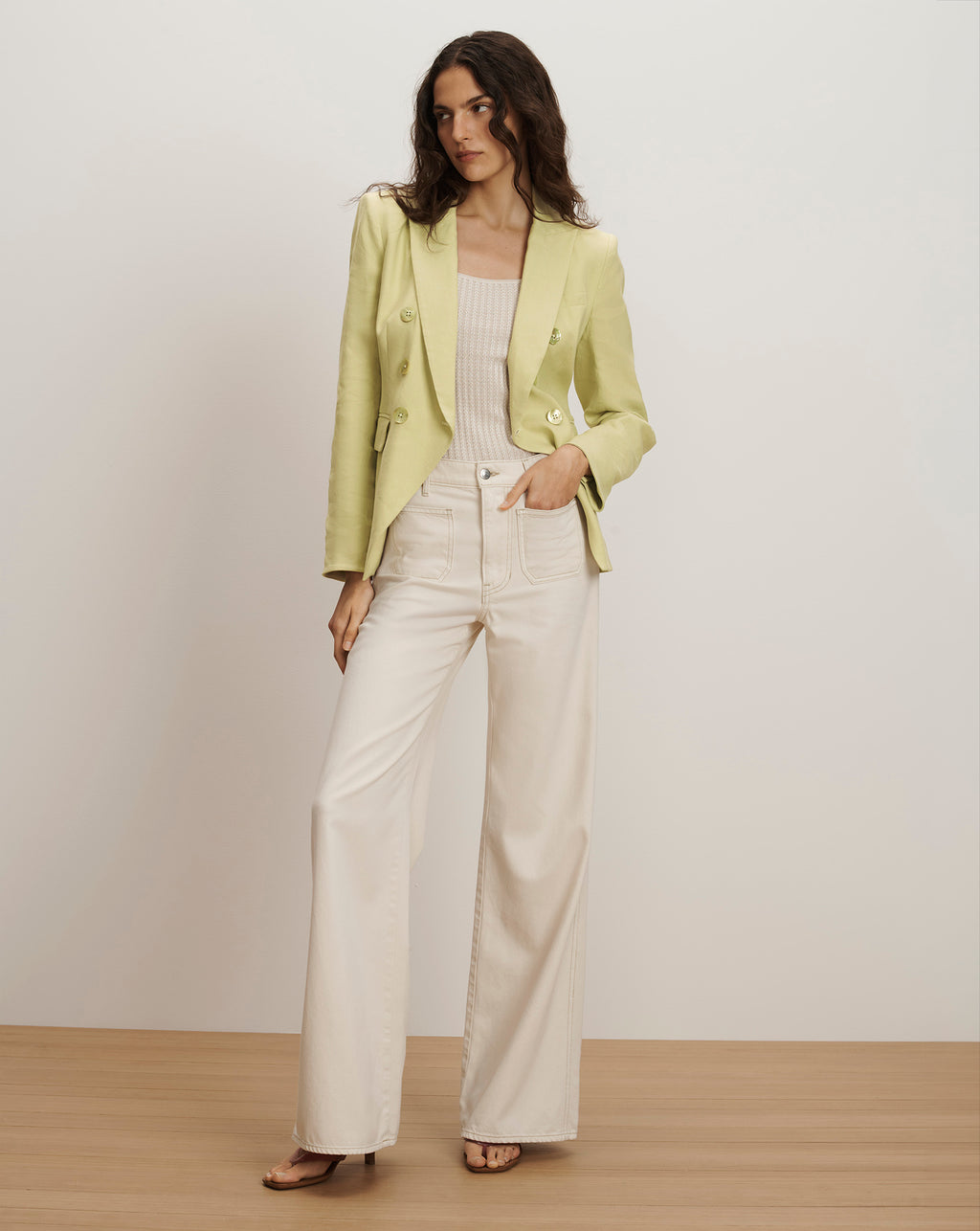 Veronica Beard Light green double-breasted blazer with gold buttons, paired with a cream ribbed tank top and off-white wide-leg jeans.