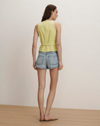 Veronica Beard Lime green sleeveless linen vest with a belted waist and light wash denim shorts.