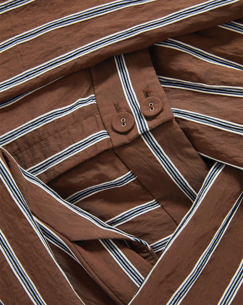 A close-up view of a brown and white striped fabric, with visible buttons and folds in the material.