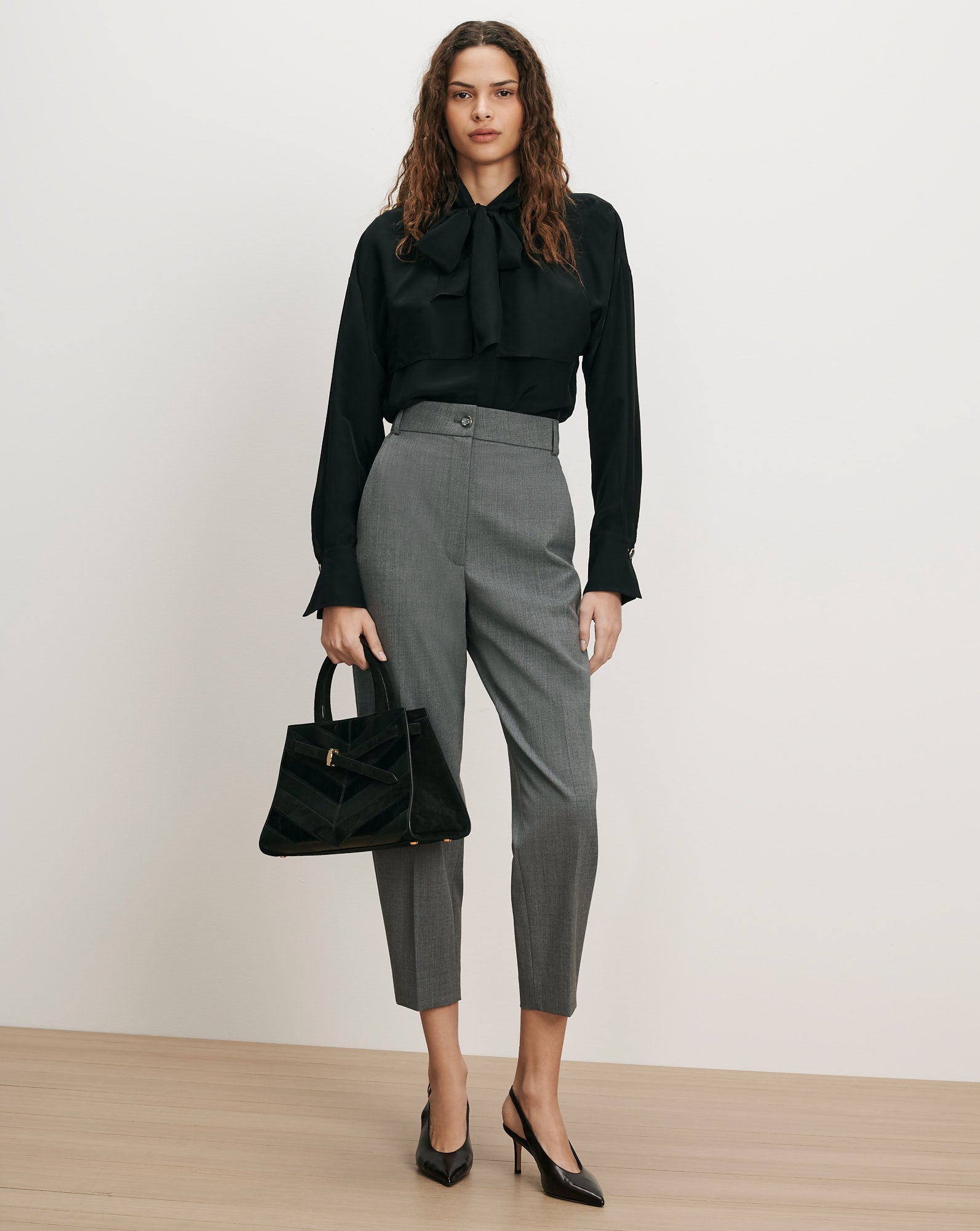 Veronica Beard Black silk bow blouse, gray wool trousers, black leather handbag.