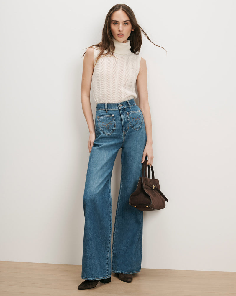 Veronica Beard Cream knit turtleneck, blue wide-leg jeans, brown suede handbag.