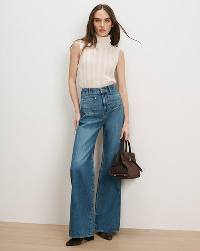 Veronica Beard Cream sleeveless turtleneck, blue wide-leg jeans, brown suede handbag.