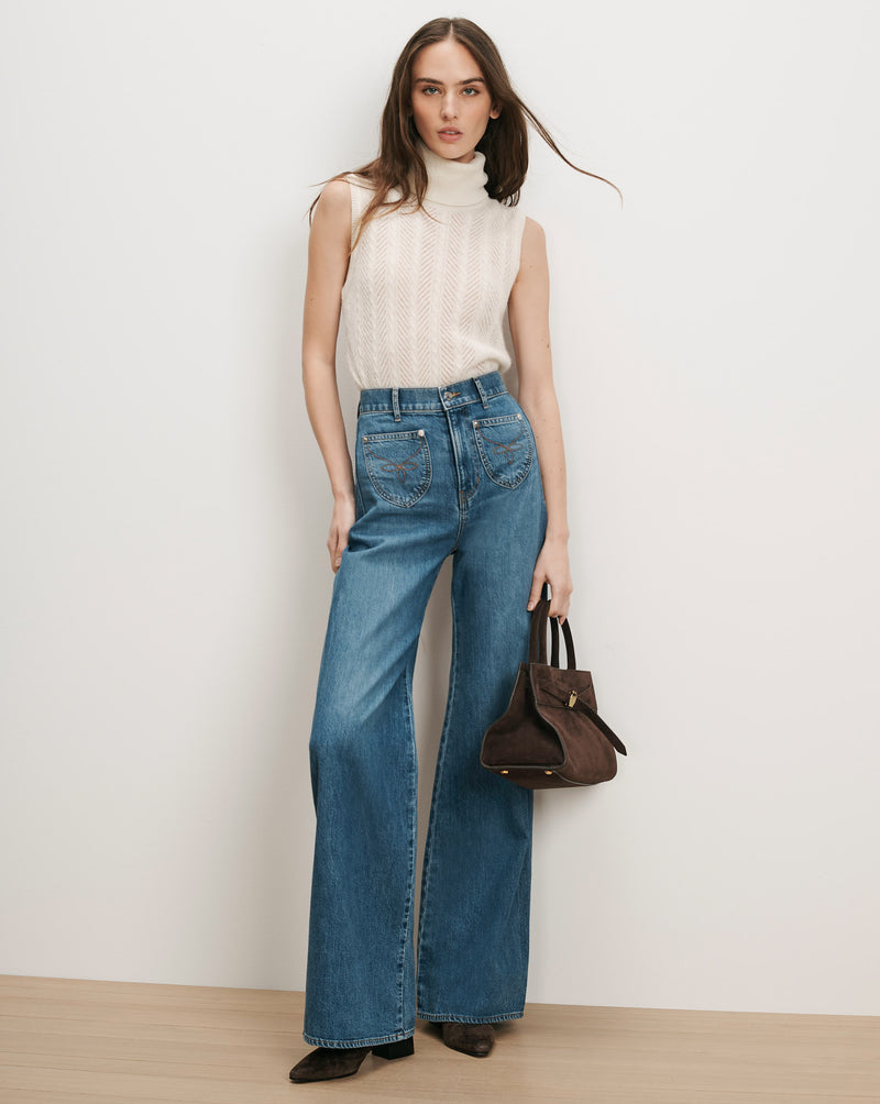 Veronica Beard Cream sleeveless turtleneck, blue wide-leg jeans, brown suede handbag.