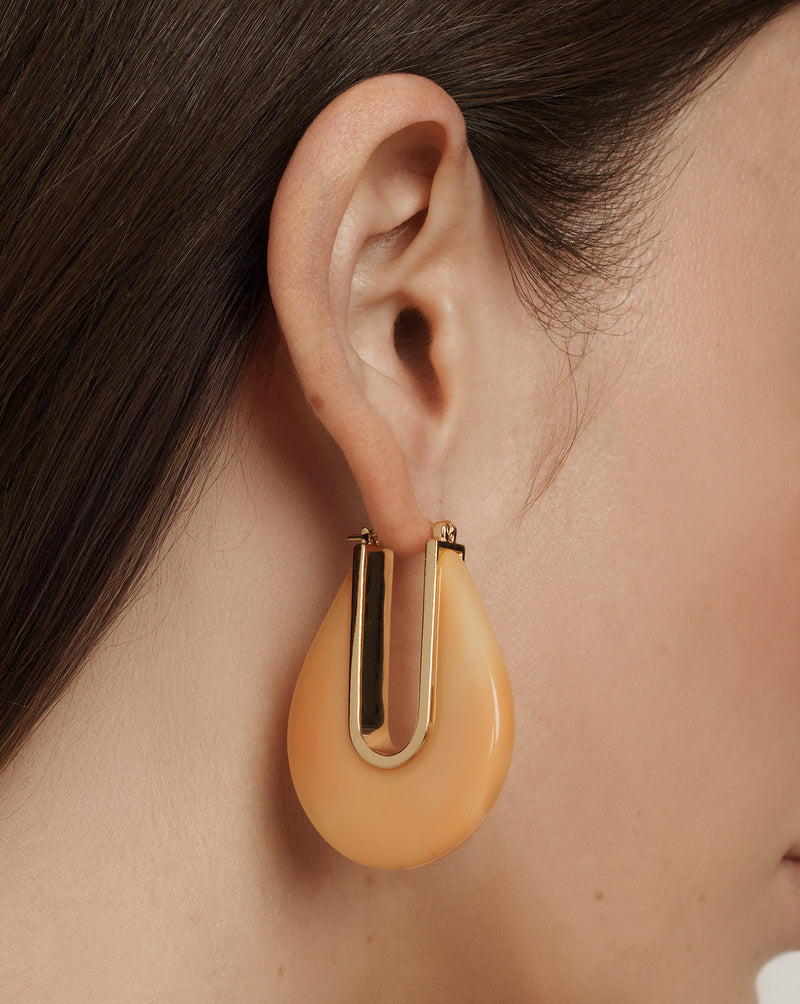 Veronica Beard A large, teardrop-shaped earring with a glossy peach-colored resin body and a gold-toned U-shaped metal insert.