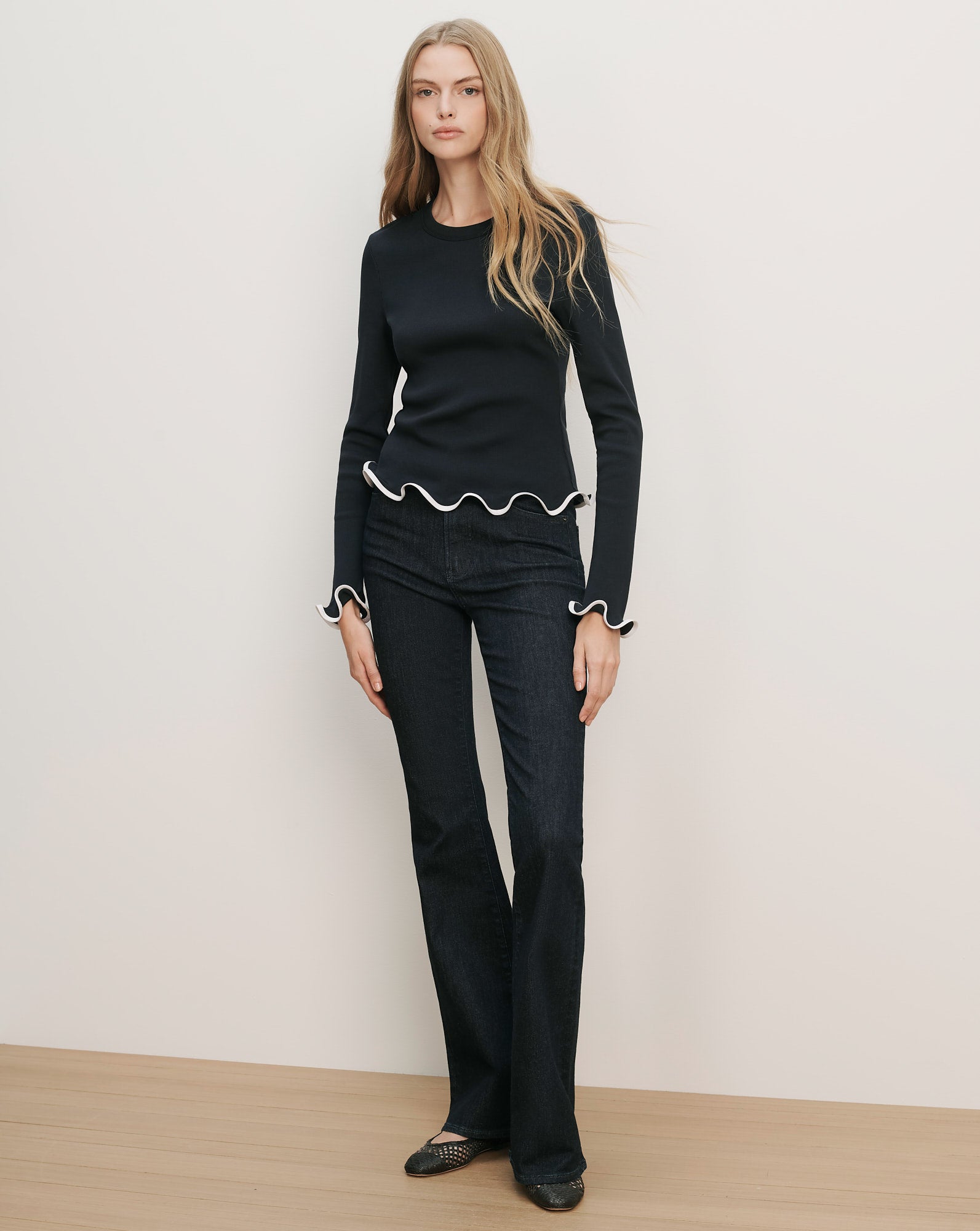 Veronica Beard Navy blue long-sleeve top with white ruffled trim on the hem and cuffs, paired with dark wash flare jeans.