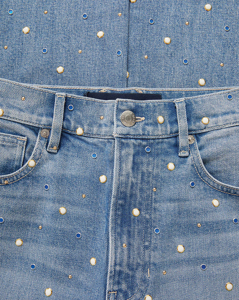 A close-up view of a pair of faded blue jeans with scattered white polka dots, revealing the denim texture and metal hardware of the waistband.