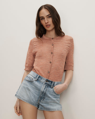 Veronica Beard Ribbed knit button-up cardigan in peach with short sleeves and light wash denim shorts.