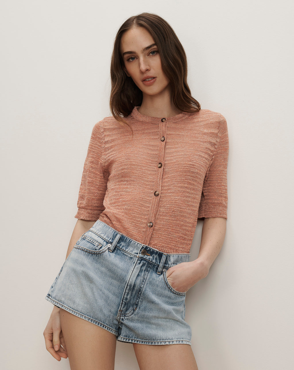 Veronica Beard Ribbed knit button-up cardigan in peach with short sleeves and light wash denim shorts.
