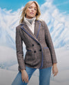 A young woman wearing a plaid jacket stands in front of a snowy mountain landscape.