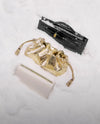 The image shows a black rectangular object, possibly a wallet or clutch, alongside a crumpled gold-colored fabric and a white rectangular object, all resting on a marble or stone surface.