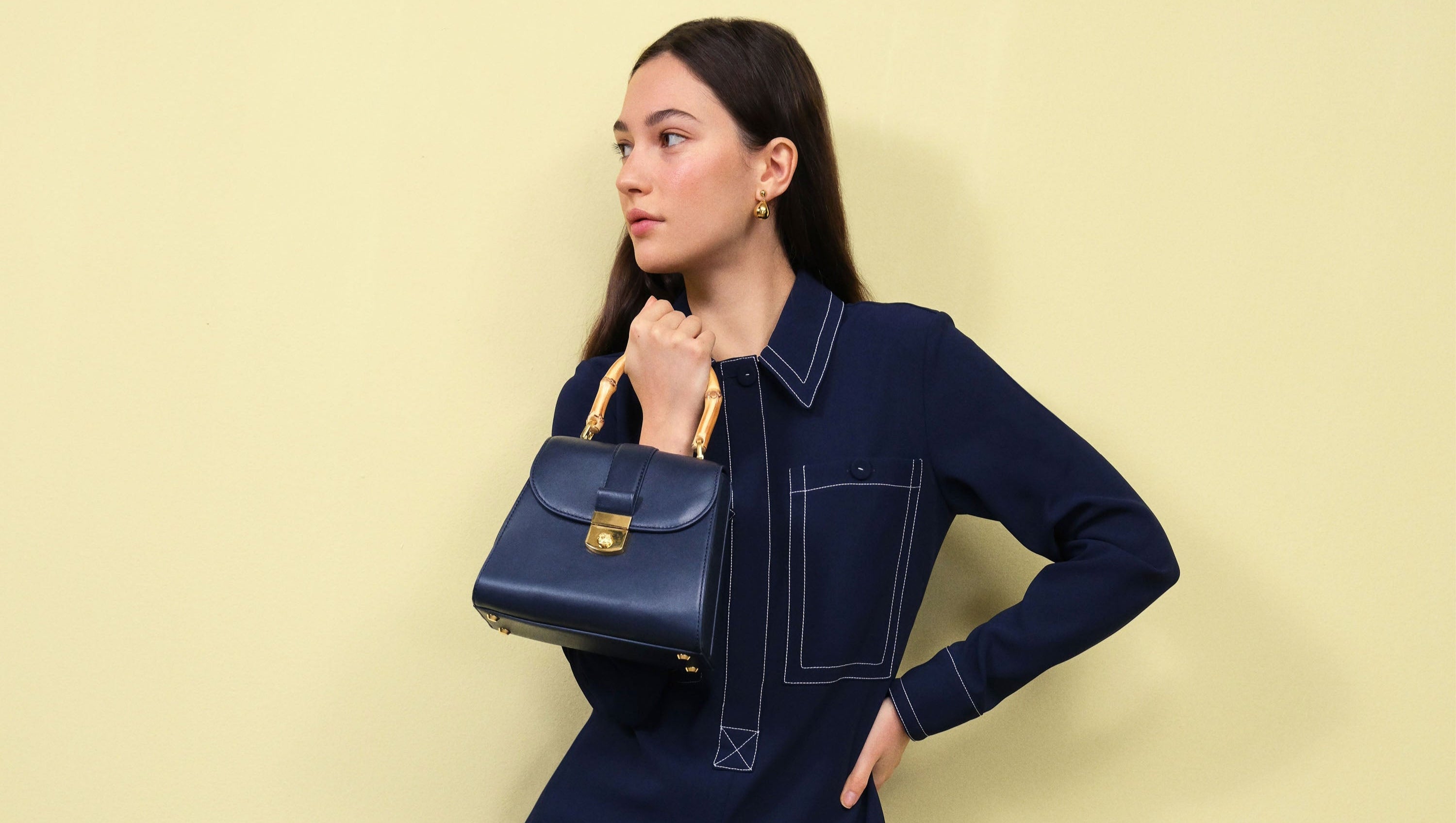 Woman holding a blue handbag against a light yellow background